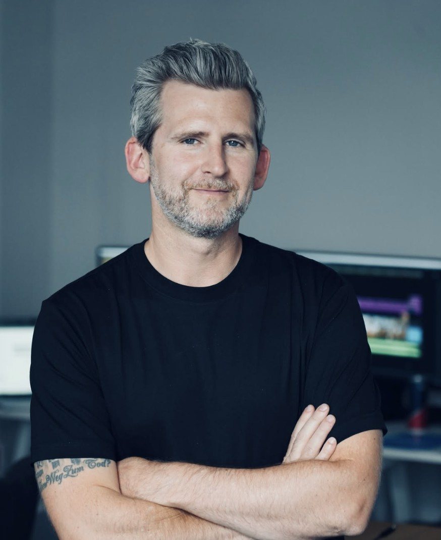 Michael Plank im Studio, die Arme verschränkt, im Hintergrund Schnittbildschirme